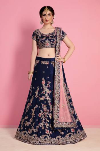 Prefect picture of grace, Bound to fall in love with this elegant yet chic navy blue color silk velvet lehenga choli look featuring dori applique floral work all over lehenga with heavy scattered sequins and stone work on hem completes the look. It comes along with embroidered butta work scattered all around Pastel pink soft net base dupatta.
