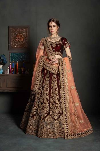 Get Ready For Your Big Day With This Latest Bridal Trend, Wearing This Heavy Designer Lehenga Choli In Maroon Color Paired With Contrasting Peach Colored Dupatta. This Heavy Embroidered Lehenga Choli Is Fabricated On Velvet Paired With Net Fabricated Dupatta. It Is Beautified With Heavy Embroidery and Stone Work. Buy Now