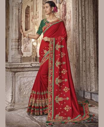 Here Is A Traditional and Evergreen Color Pallete With This Heavy Designer Saree In Red Color Paired With Contrasting Green Colored Blouse. This Saree And Blouse Are Silk Based Beautified With Heavy Embroidery. 